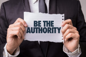 Man in a suit holding a piece of paper that says "Be the authority"