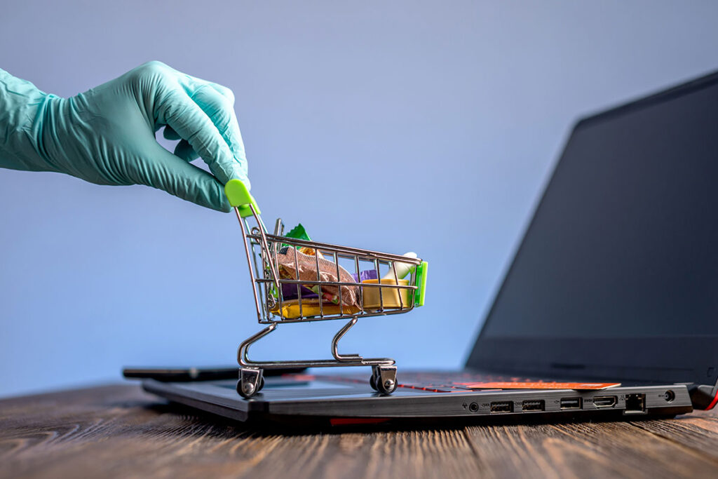 the hand of a surgeon grabbing a tiny market shopping cart on a laptop in relation to medical product pages.