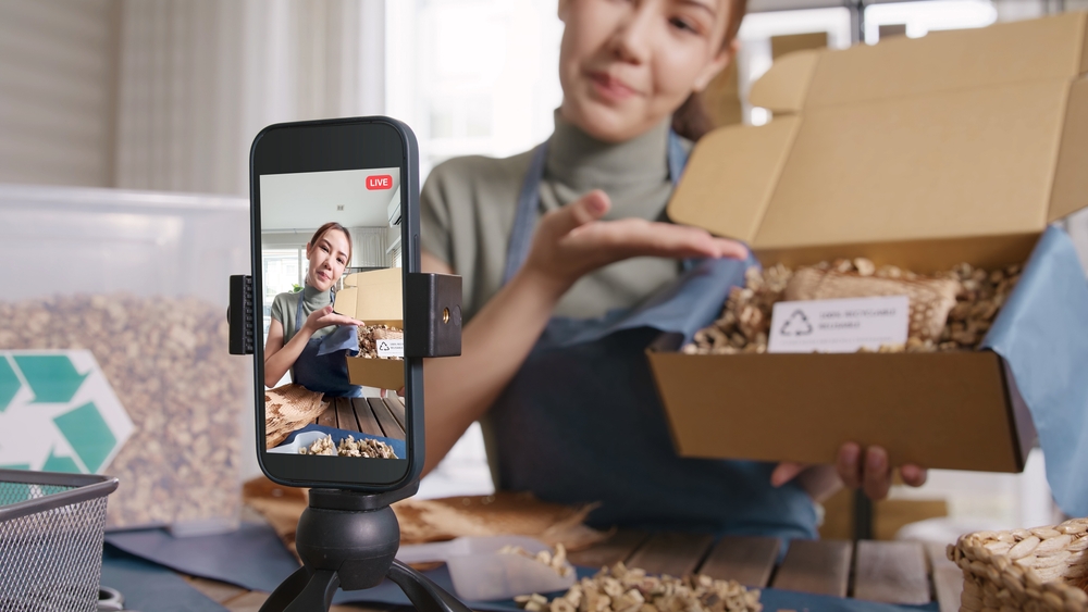 A woman is live streaming an unboxing video on Instagram, engaging with viewers and showcasing a product.