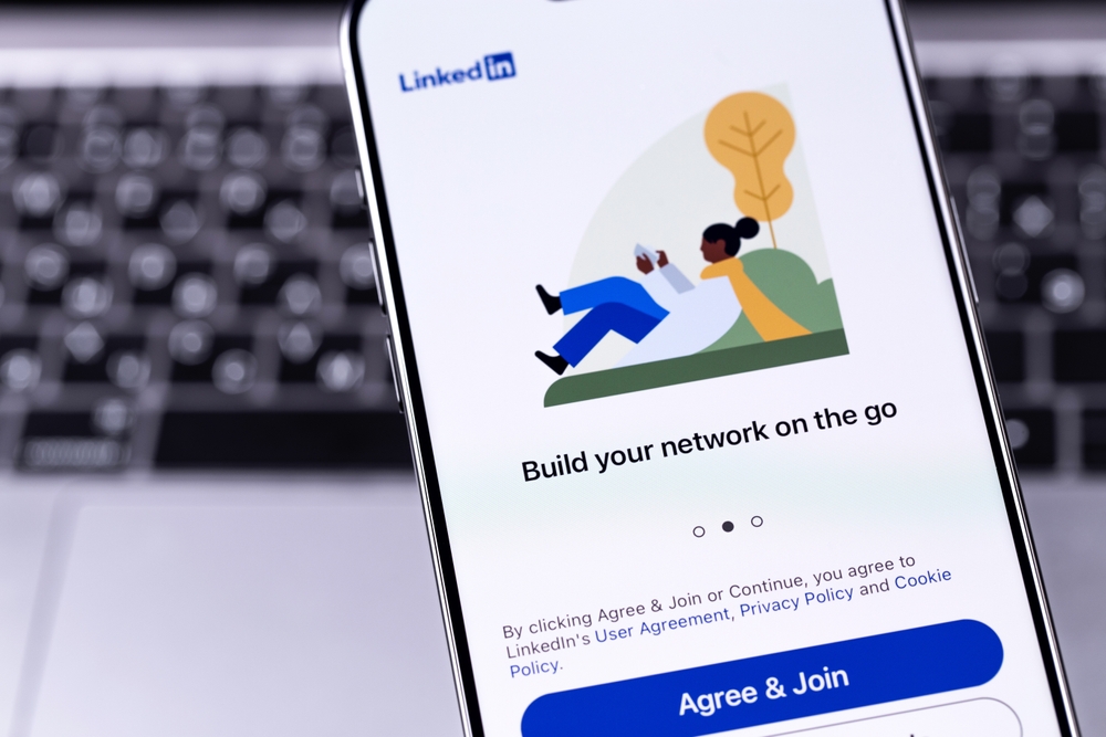  LinkedIn app on a phone screen with networking graphics, above a laptop keyboard.