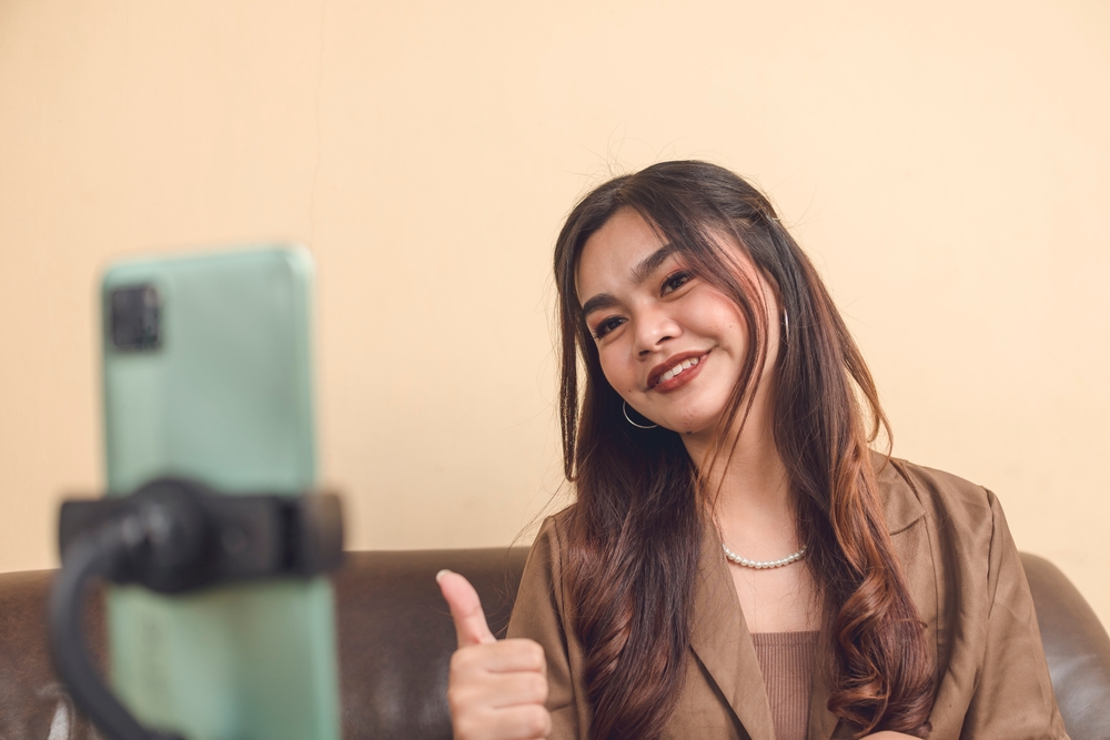 A woman gives a thumbs up to her phone camera, likely creating content for platforms like YouTube or YouTube Shorts.