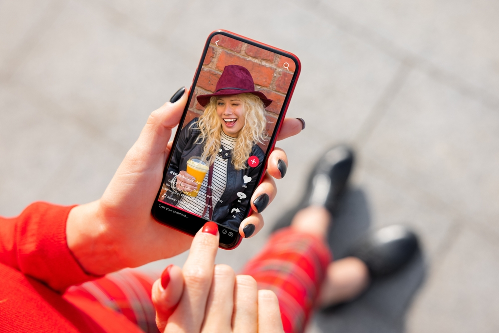 Smartphone displaying a TikTok video of a woman laughing and holding a drink, reflecting engagement with trend-driven content on the platform.