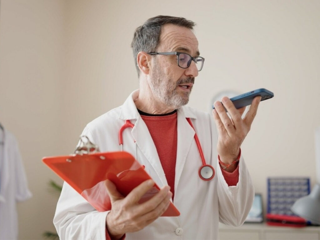 Doctor consulting clipboard while speaking into smartphone, highlighting voice search SEO.